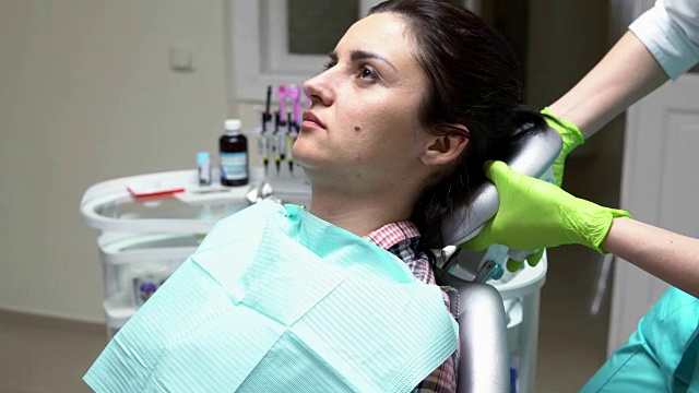 年轻的女病人坐在牙医的椅子上，准备检查。女医生帮助感觉舒适。在4 k拍摄视频素材