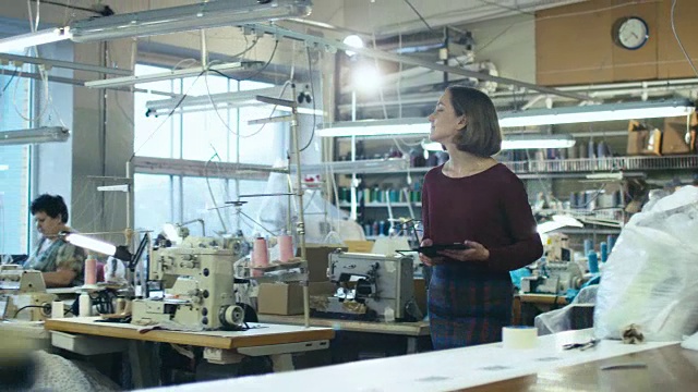 一位手持平板电脑的年轻女性正走过一家服装厂。视频素材