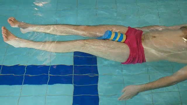 这个人在游泳池里慢慢地游泳，两腿之间放着运动器材视频下载