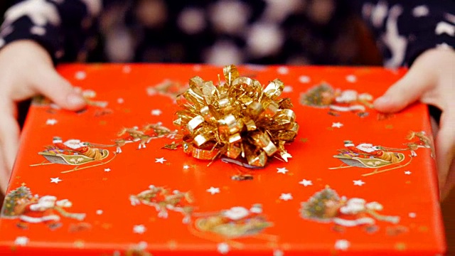 特写的两个孩子的手拿着一个美丽的彩色包装纸与一个金色的蝴蝶结圣诞礼物视频下载