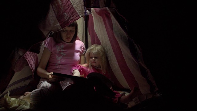 妈妈和女儿晚上在帐篷里用手电筒看书。视频素材