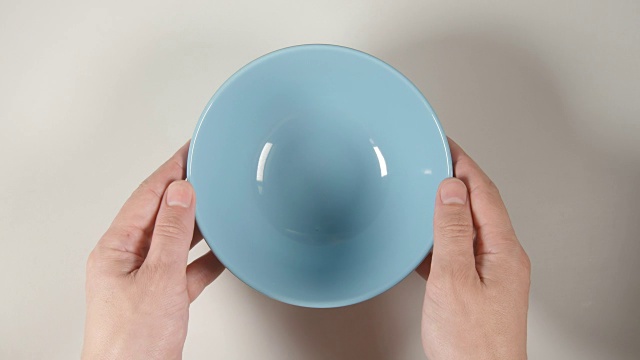 俯视图:人的手把一个蓝色的汤碗放在白色的桌子上视频下载