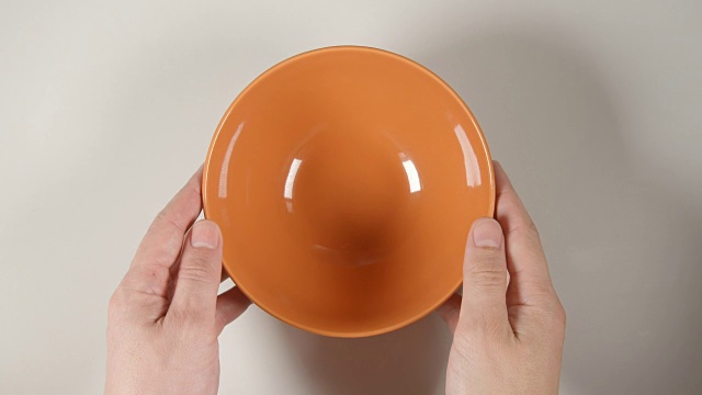 俯视图:人的手把一个橙色的汤碗放在白色的桌子上视频下载