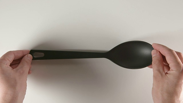 俯视图:人的手把一个黑色的塑料勺子放在一张白色的桌子上视频下载