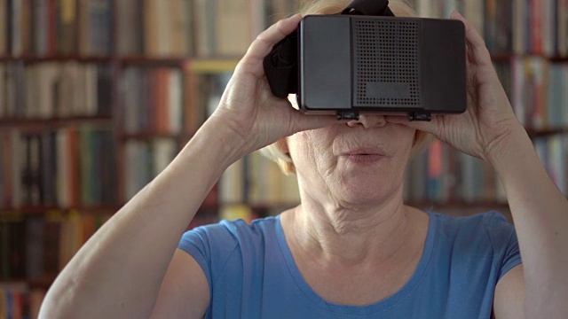 现代高级女性在家使用虚拟现实眼镜。书架的背景视频素材