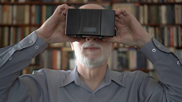 现代老年人在家使用虚拟现实眼镜。书架的背景视频素材