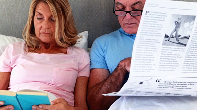 一对老年夫妇在床上读报纸和书视频素材