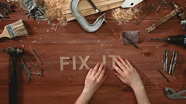俯视图延时拍摄的一只手放在木桌上，上面写着“FIX IT”视频下载