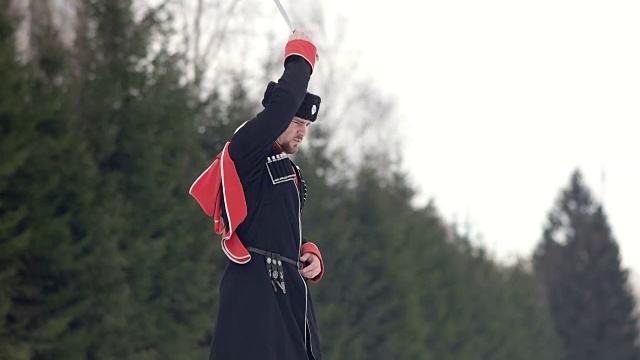 一个穿着哥萨克衣服的年轻人在雪地里挥舞着一把剑。视频下载