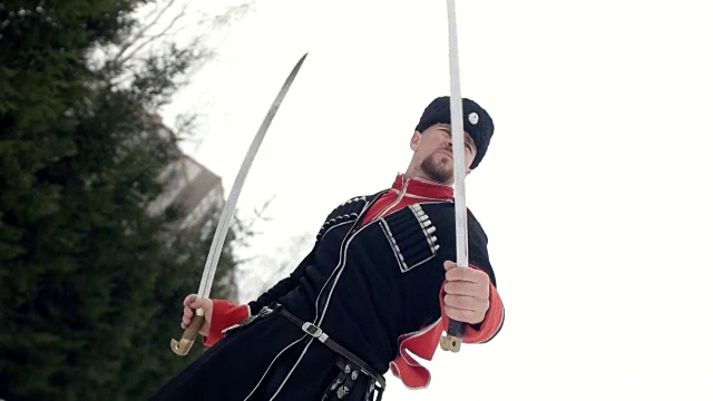 一个穿着哥萨克衣服的年轻人在雪地里挥舞着一把剑。视频下载