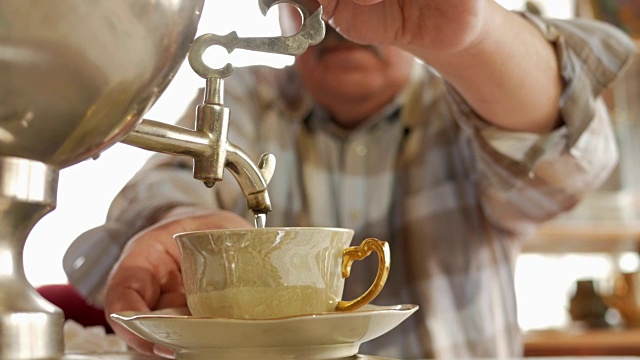 一对老夫妇正在用一个古老的俄罗斯茶壶沏茶。一个留着胡子的男人为他的妻子倒茶视频下载