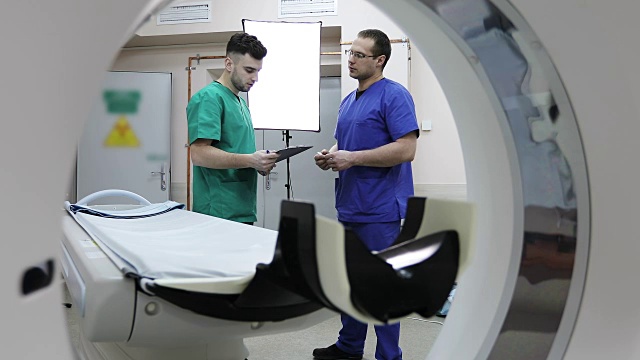 两个年轻的医生在一个房间里用CT扫描仪讨论病人的治疗。视频素材