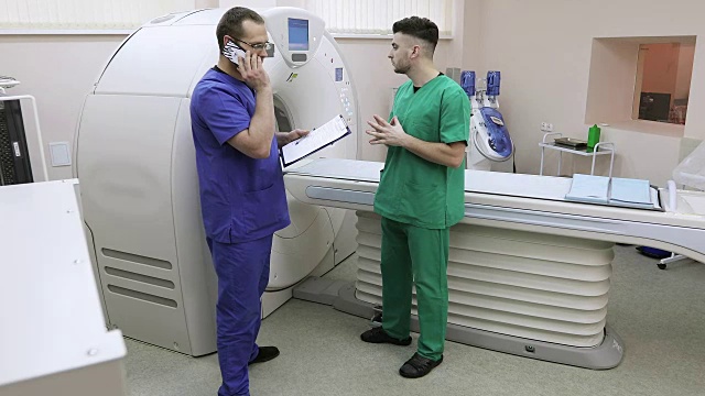两个医生在一个房间里拿着一台CT扫描仪。这位年轻的专家用手机进行咨询。视频素材