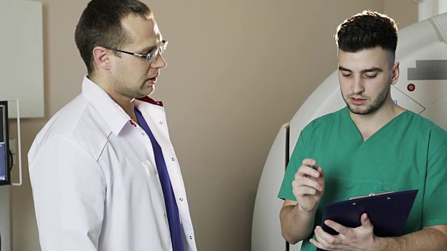 两名身穿医疗服的年轻医生在一个诊所的柜式CT扫描仪中交谈。视频素材