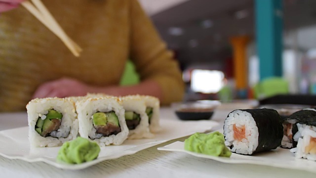 女孩坐在咖啡馆的桌子上，用木棒叼着一个绿色的芥末寿司，日本料理视频素材