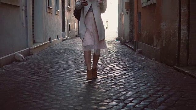 近距离观看年轻女子走在阳光明媚的春天城市街道在欧洲。时尚女孩独自探索古城视频素材