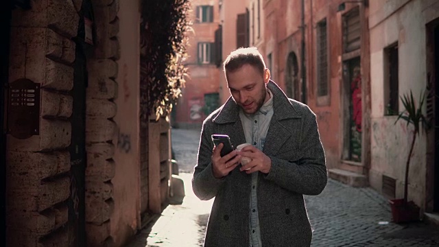 年轻帅气的男人走在城市里，用着智能手机。男性与朋友聊天，喝咖啡视频素材