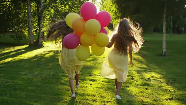 日落时分，双胞胎女孩手拿气球在公园里奔跑视频下载