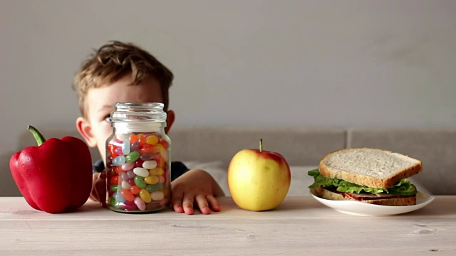 可爱的小男孩把五颜六色的糖果放在罐子里视频素材