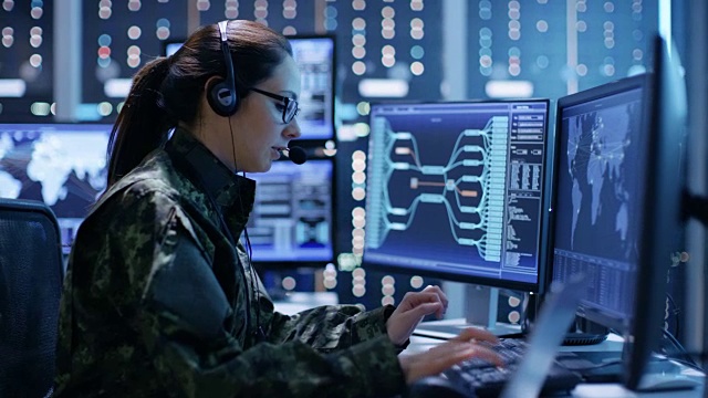 女军事技术支持专业人员给耳机指令。她在一间有很多工作屏幕的监控室里。视频下载