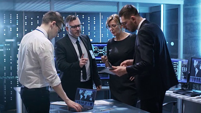 政府官员小组在监控室进行建设性讨论。一名男子手持平板电脑，桌上放着笔记本电脑。电脑有动画屏幕。视频素材
