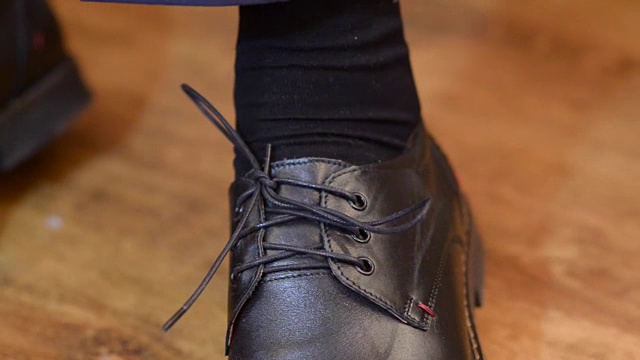 男人把他的鞋带系在他的黑鞋子上，男人穿着白衬衫和深色裤子视频素材