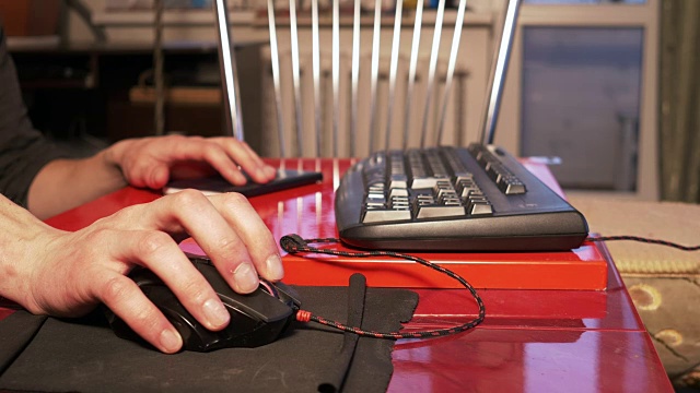 一个年轻人坐在家里的桌子旁用电脑鼠标视频下载