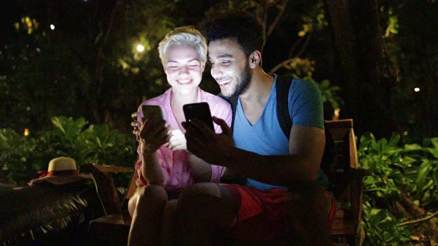 情侣用手机拥抱，坐在傍晚公园的长椅上，男女在户外网上聊天视频素材