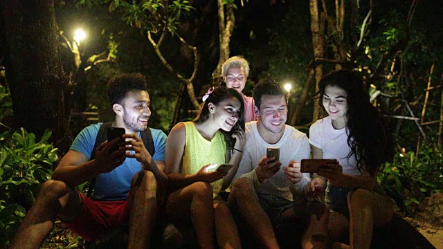 人们在晚上公园的长椅上用手机聊天，年轻的朋友在网上聊天视频素材