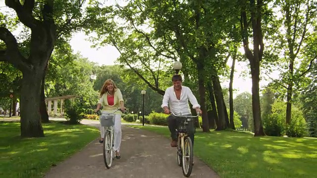 快乐的成人夫妇在公园里骑自行车。视频下载