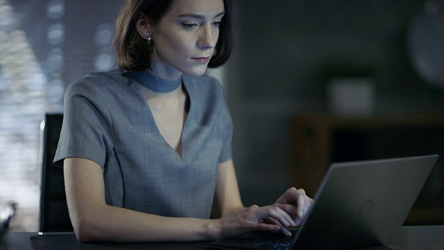 时尚的女性高管在私人办公室里用笔记本电脑工作。她的工作空间是现代的，暗色调的，从窗户看出去的大城市。视频素材