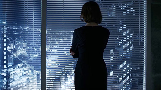 在一个现代的办公室女商人深思地看着窗外的大城市。视频素材