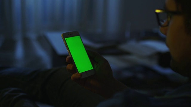 男人晚上躺在沙发上，用绿色屏幕竖屏的手机。视频素材