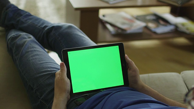 男人躺在家里的沙发上，在平板电脑上看风景模式的绿屏视频下载