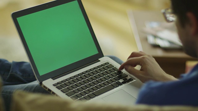 一名男子躺在沙发上使用绿色屏幕的笔记本电脑视频素材