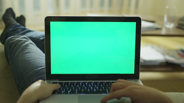 躺在家里的沙发上使用绿色屏幕的笔记本电脑。视频素材