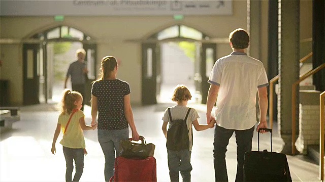 一个幸福的家庭，小女孩和小男孩要去火车站，爸爸妈妈和孩子们带着行李箱走过机场视频素材