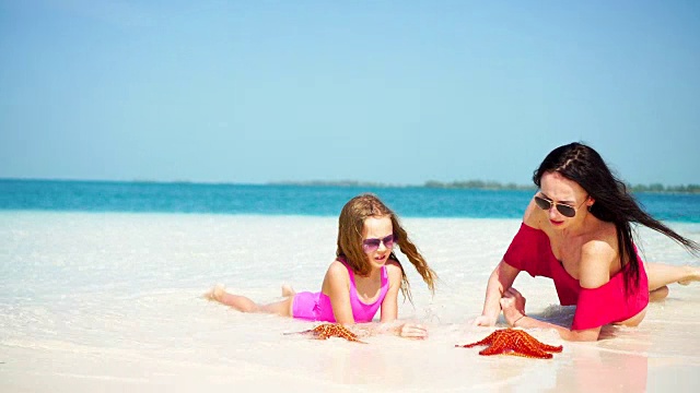 可爱的小女孩和年轻的母亲在热带海滩躺在白色的海滩上，享受他们的暑假视频素材