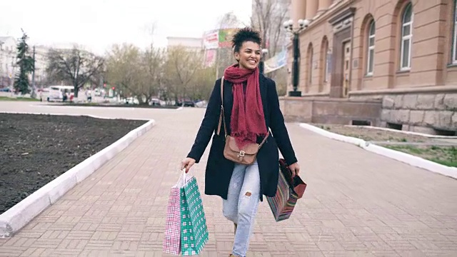 多莉拍摄的迷人的混血女孩跳舞和有乐趣，而走在街上的袋子。快乐的年轻女子走在购物中心出售视频素材