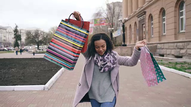 多莉拍摄的迷人的混血女孩跳舞和有乐趣，而走在街上的袋子。快乐的年轻女子走在购物中心出售视频素材