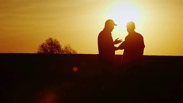 两个农民在田地里坚定地握手。他们用平板电脑交流。在日落时视频下载
