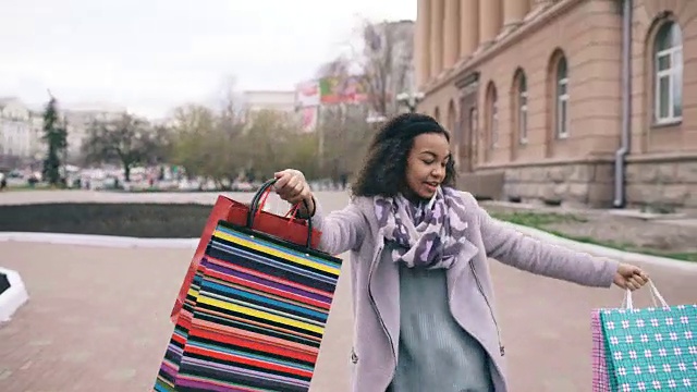 迷人的混血女孩跳舞和有乐趣，而走在街上的袋子。快乐的年轻女子走在购物中心出售视频素材