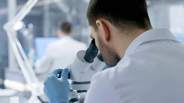 从一个研究科学家的肩膀看显微镜。他和他的同事在现代实验室进行实验。视频素材