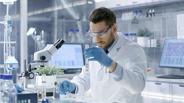 在一个现代实验室生物学家进行实验合成化合物使用滴管和植物在一个试管。视频素材