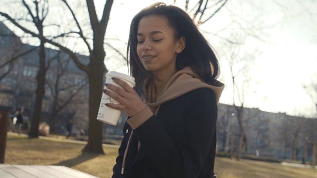 在阳光明媚的日子里，时尚的女人在城市公园里喝着咖啡放松。视频素材