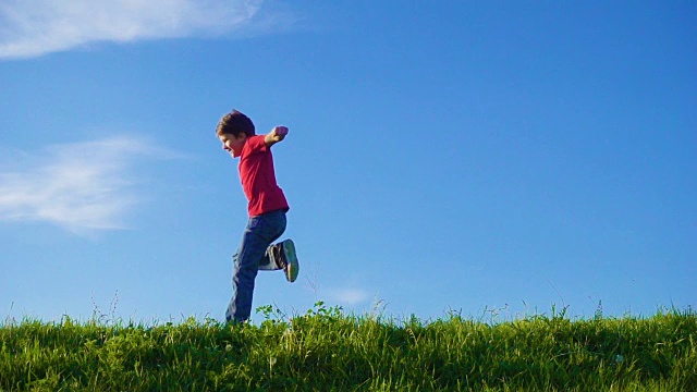 快乐的小男孩在碧绿的草山上奔跑，对着蓝天视频素材