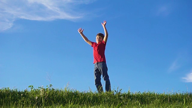 快乐的男孩跳跃在绿色的草山上，对着蓝天视频素材