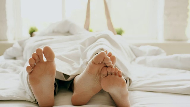 年轻美丽和相爱的夫妇的特写拥抱和玩他们的脚下的毯子，而在床上醒来在早上视频素材