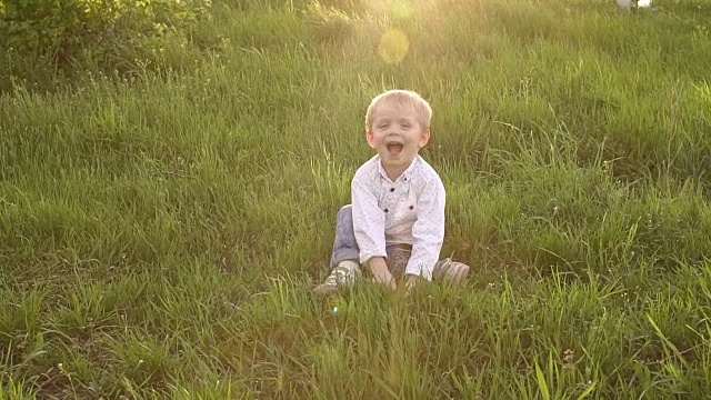 快乐的小男孩坐在公园的草地上。视频素材