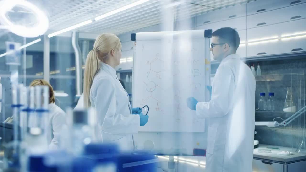 年轻的男女科学家在白板上写公式。他们在光明现代高科技实验室里解决科学问题。视频素材